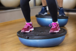 Low section of woman standing on bosu ball in health club
