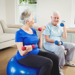 Senior couple sitting on fitness balls with dumbbells