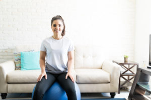 Portrait of smiling young woman sitting on a swiss ball for exercising in her living room