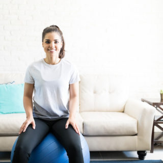 Portrait of smiling young woman sitting on a swiss ball for exercising in her living room