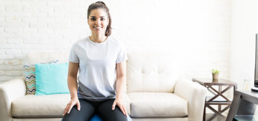Portrait of smiling young woman sitting on a swiss ball for exercising in her living room