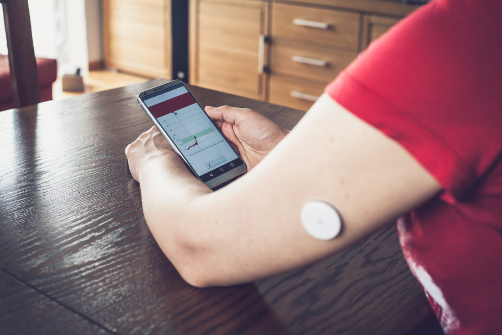 Woman checking glucose level with a remote sensor and mobile phone, sensor checkup glucose levels without blood. Diabetes treatment. Focus on background