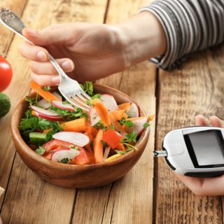 Woman holding digital glucometer while eating salad at table. Diabetes diet