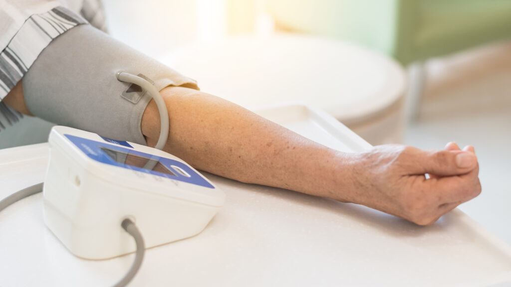 Patient checking up blood pressure using upper arm blood pressure measuring monitor medical equipment in clinic examination room