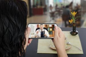 Woman sits at a cafe table and communicates with telemedicine doctor by cellphone. In touchscreen, male physician reviewing brain x-ray image.