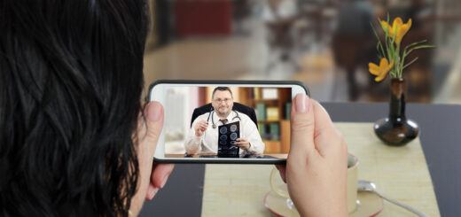 Woman sits at a cafe table and communicates with telemedicine doctor by cellphone. In touchscreen, male physician reviewing brain x-ray image.
